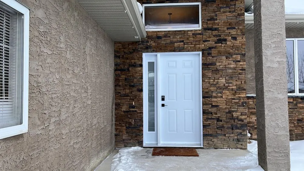New white six-panel entry door with a narrow sidelite, set in a stone wall, with snow on the step